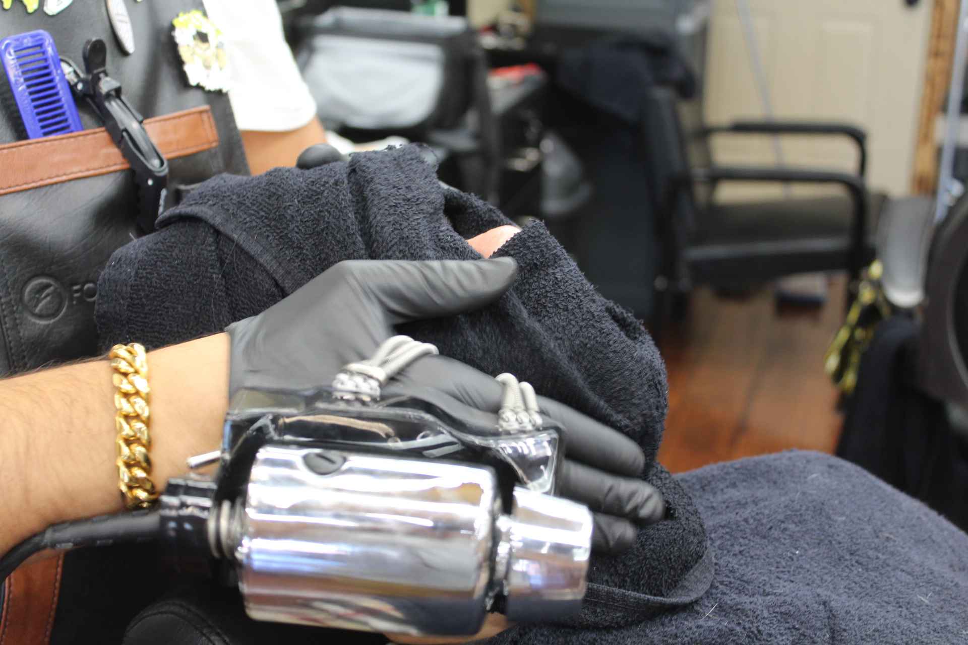 A gloved barber pressing a hot towel, with the towel steamer in the foreground